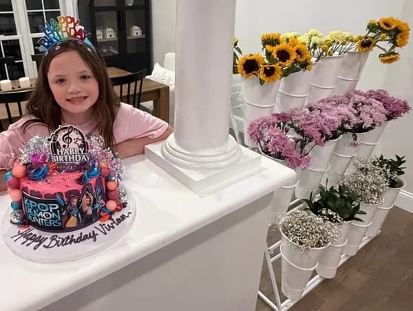 Girl smiling beside a birthday cake and a tiered display of flower buckets.